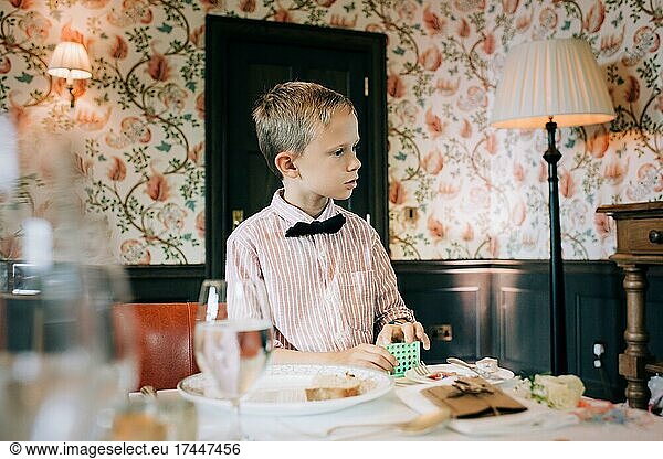 boy dressed in a shirt and bow tie playing at a wedding