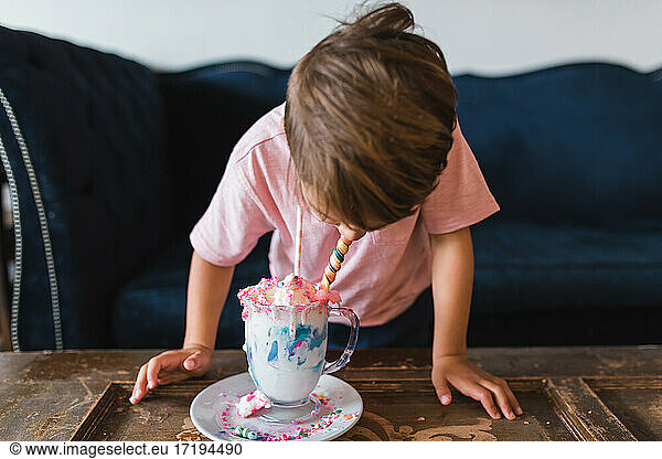 Boy drinking a colorful milk shake in front of a vintage blue couch.