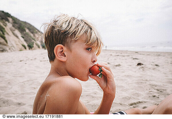 Boy Eating a Strawberry on a Sandy Beach in California