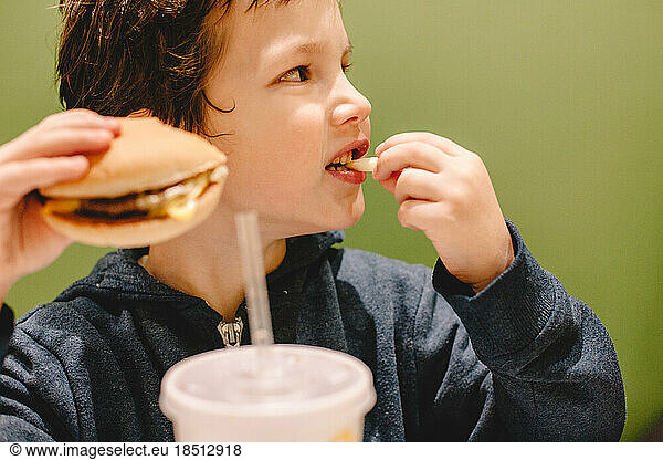 Boy eating french fries and burger while sitting at restaurant