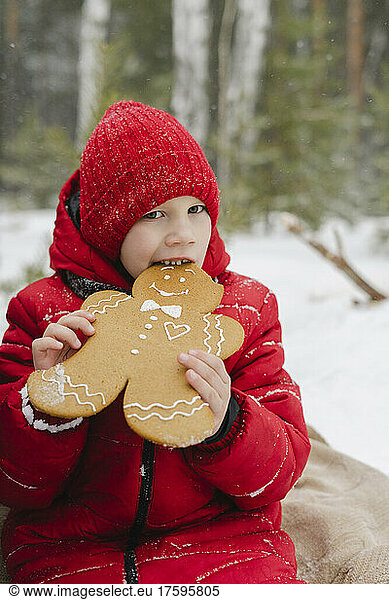 Boy eating gingerbread cookie sitting in winter