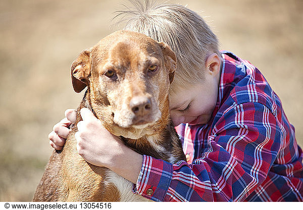 Boy embracing dog on field