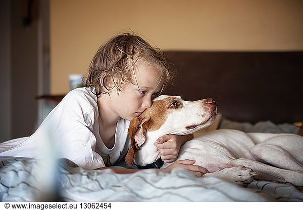 Boy embracing dog while lying on bed at home