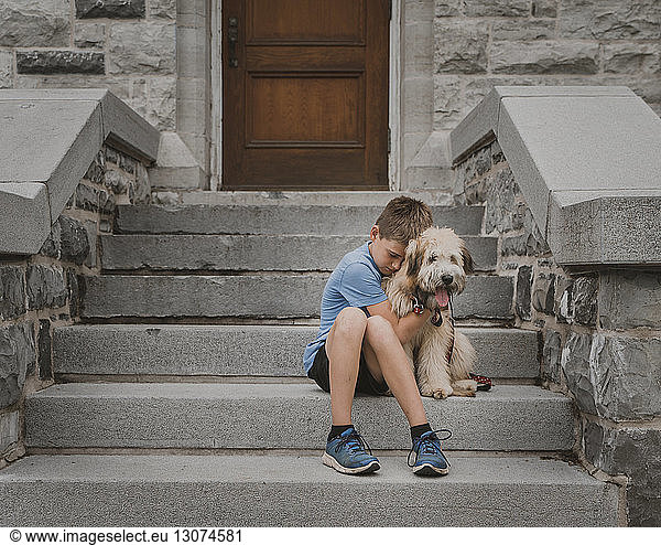 Boy embracing dog while sitting on steps