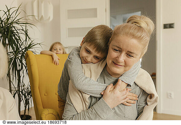 Boy embracing grandmother sitting at home