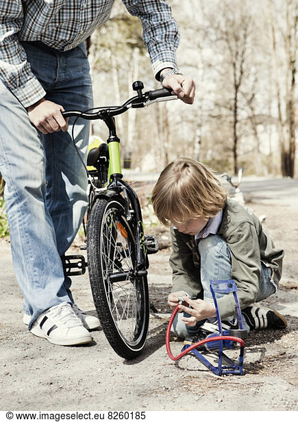 Boy filling bicycle tire with foot pump while father standing on road