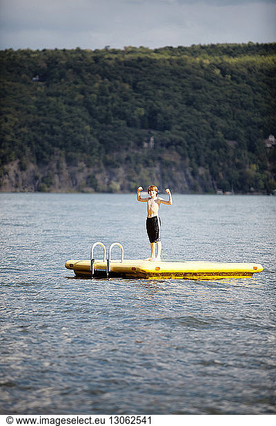 Boy flexing muscles while standing on floating platform in lake