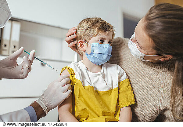 Boy getting vaccinated by doctor with mother at center