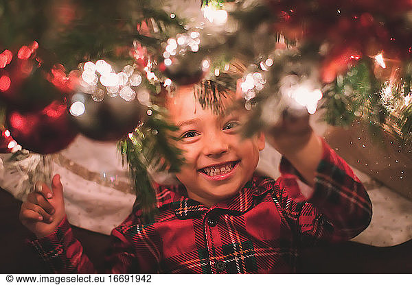 Boy hanging looking at camera under the Christmas Tree at night time