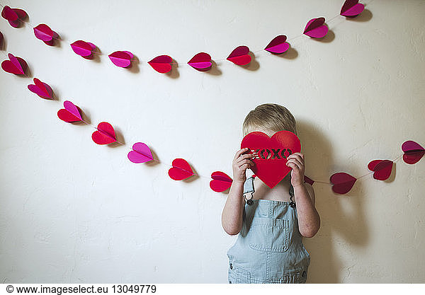 Boy hiding face with heart shape while standing against wall