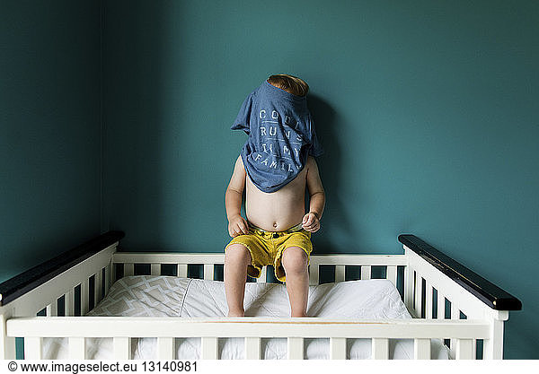 Boy hiding face with t-shirt while sitting on railing