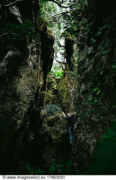 Boy hikes and climbs up a cliff in a tropical forest