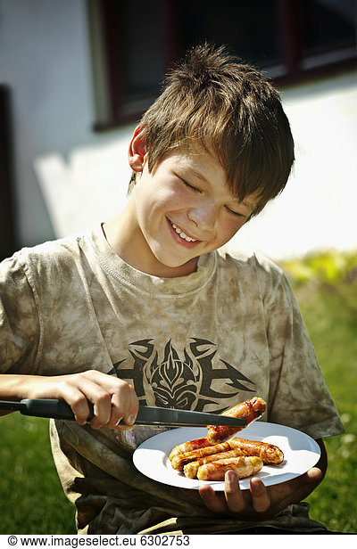 Boy holding a plate with grilled sausages