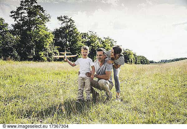 Boy holding airplane toy while playing with father and mother at meadow