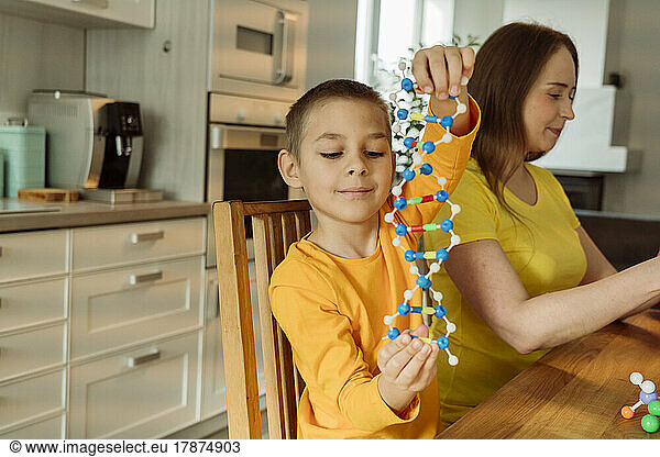 Boy holding DNA model by mother at home