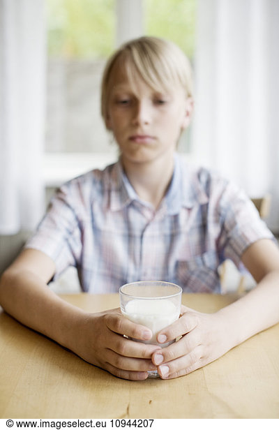 Boy holding drinking glass with milk on table
