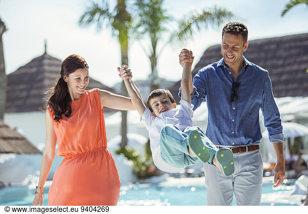Boy holding hands with his parents by swimming pool