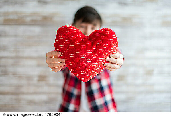 Boy holding heart pillow in front of him with blurred background.
