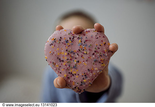 Boy holding heart shape sweet food at home
