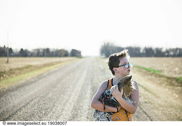 Boy holding his pet puppy in the country on a gravel road.