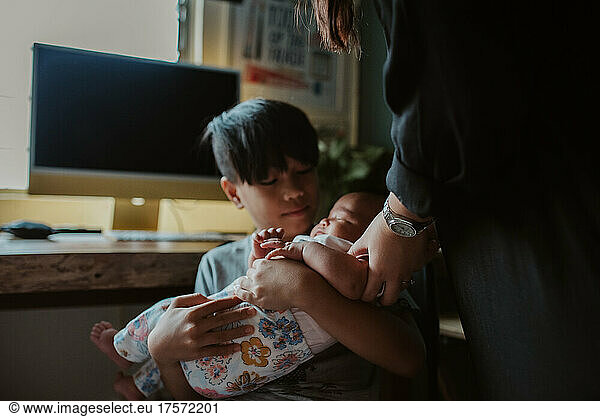 Boy holding newborn girl at home
