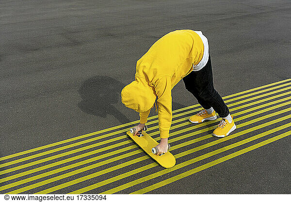 Boy holding skateboard while bending over yellow markings on road