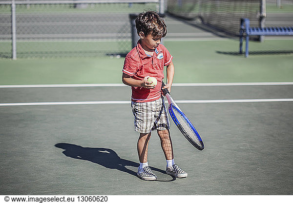 Boy holding tennis racket and ball while standing on court