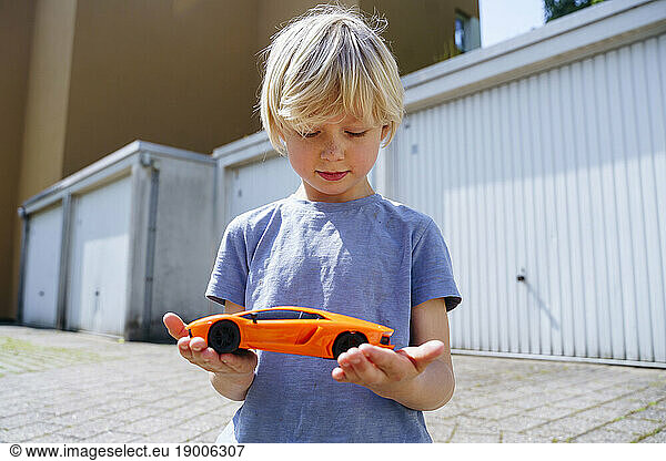 Boy holding toy car in yard outside garage