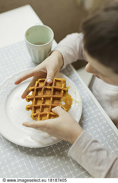 Boy holding waffle on dining table in kitchen