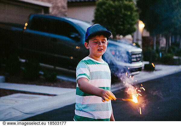 Boy holds a sparkler fire work on July 4th in the dark in neighborhood