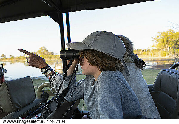 Boy in a safari jeep looking through binoculars.