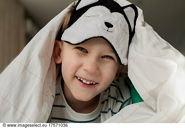boy in a sleep mask laughing under the covers