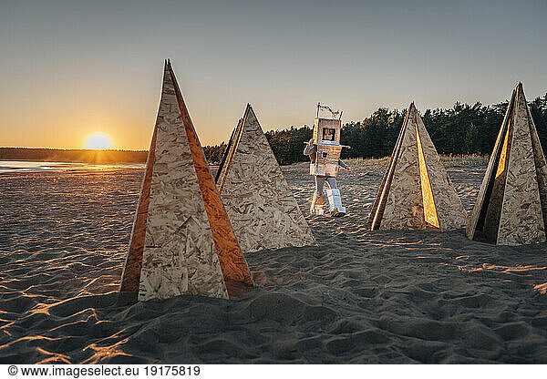 Boy in astronaut suit by futuristic tents on sand at beach