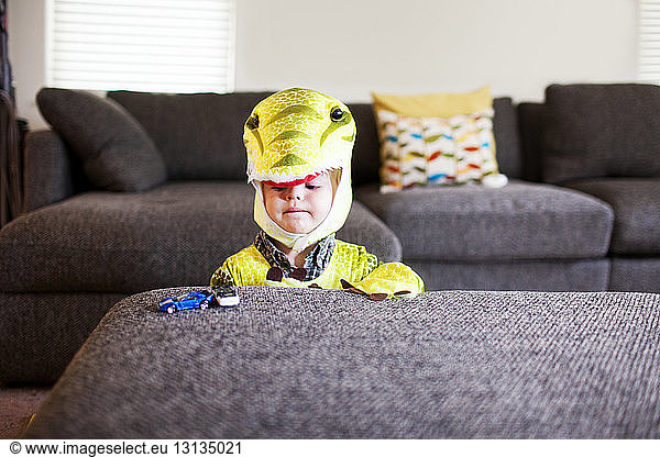 Boy in dragon costume looking at toys while sitting at home