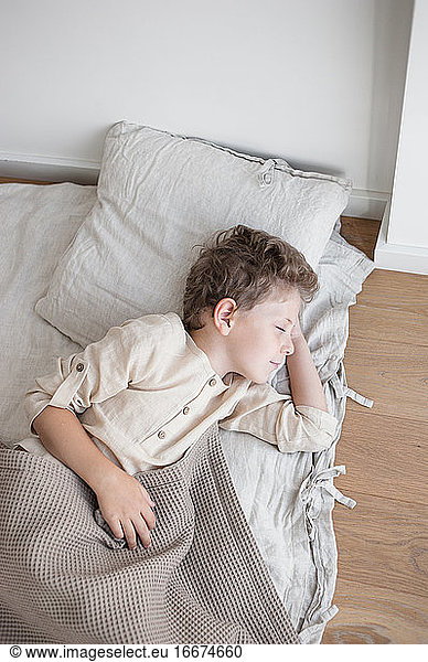 Boy in linen clothes sleeps in natural linen covered bed daytime.