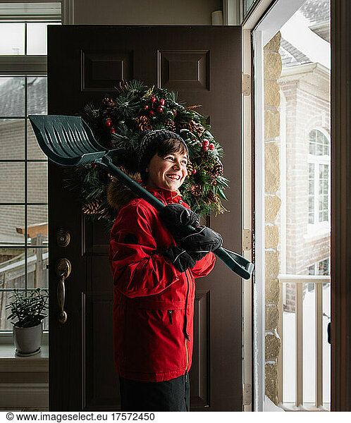 Boy in red coat with snow shovel going out the door on winter day.