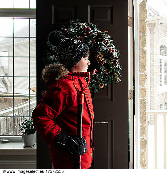 Boy in red coat with snow shovel going out the door on winter day.
