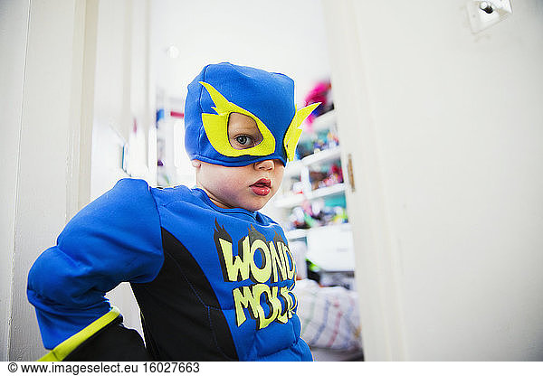 Boy in superhero costume posing in door to his room