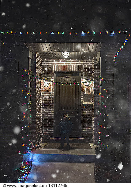Boy in warm clothing standing at entrance during night