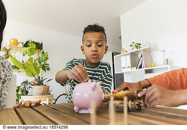 Boy inserting coin into piggy bank at home