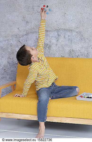 Boy is playing and experimenting with molecular models sitting on yellow couch