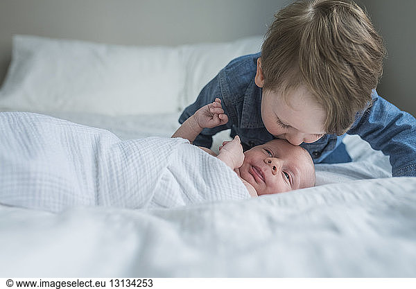 Boy kissing brother's forehead on bed at home