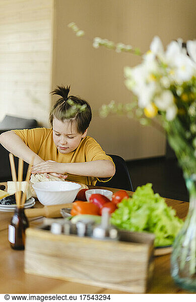 Boy kneading pizza dough on table