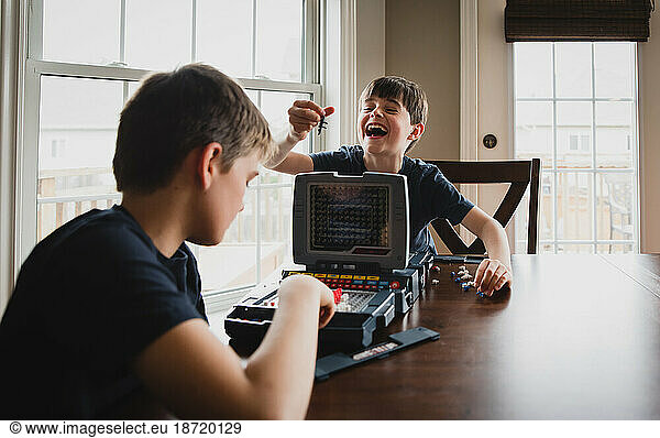 Boy laughing at his brother as they play a board game together.