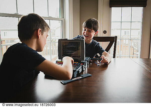 Boy laughing at his brother as they play a board game together.