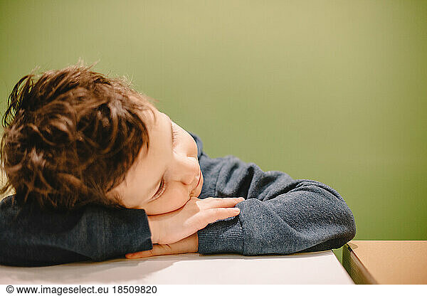 Boy leaning on desk against green background
