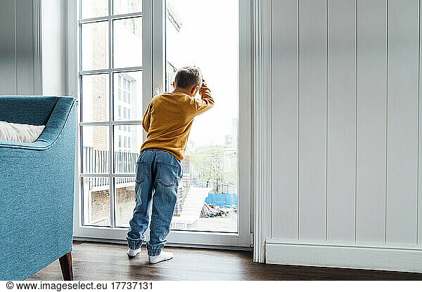 Boy leaning on glass window at home