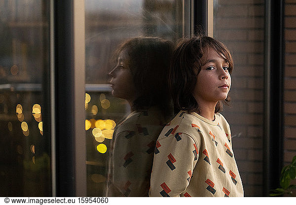 Boy leaning on window  mirrored in glass pane