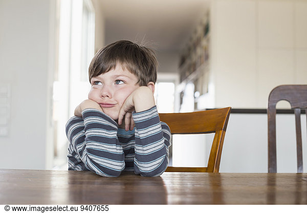 Boy leaning on wooden table  looking away