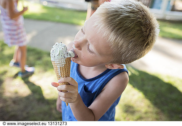 Boy licking melting ice cream while standing at backyard